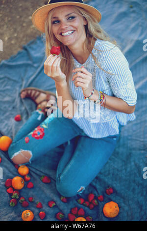 Happy young woman in hat eating strawberry on picnic in nature Stock Photo