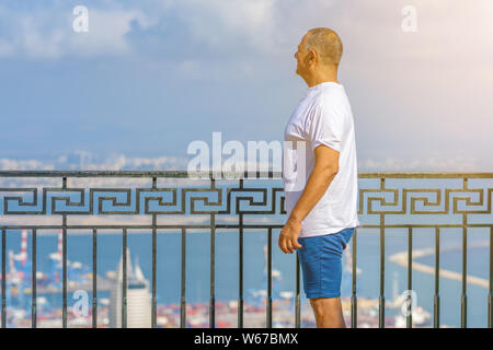 Senior athletic man standing on coastline and enjoying beautiful view over the sea. Traveling along coast, freedom and active lifestyle concept.Business man on vacation. Stock Photo
