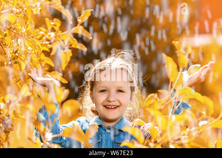 Portrait of a cute charming little girl standing in autumn park in the rain. The child stretched out his hands and collects the drops in his palm. Stock Photo