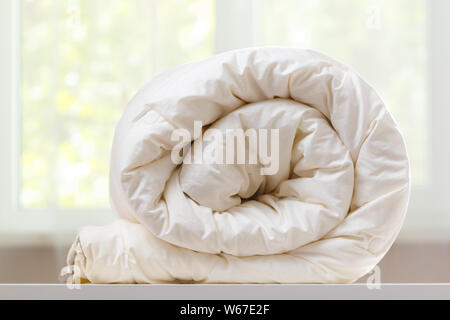 A folded rolls duvet is lying on the dresser against the background of a blurred window. Household. Stock Photo