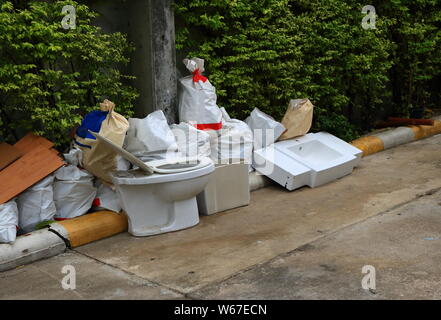 Damaged flush toilet and a pile of garbage dumped on wayside Stock Photo