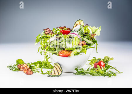Fresh vegetable salad with fried bacon tomatoes olives arugula zucchini tzatziki dressing and olive oil. Stock Photo