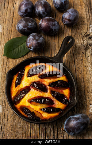 Classic golden cast iron pie and fresh purple plum on the rustic wooden background Stock Photo