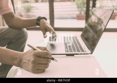 Anonymous Worker using laptop as well as writing on a sheet of paper a business project on office desk table. Side view. Close-up. Vintage style effec Stock Photo