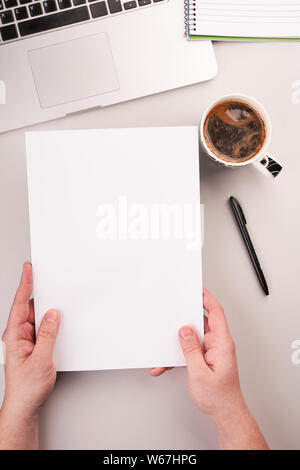 Man's hands holding blank paper on the working desk with computer and coffee Stock Photo