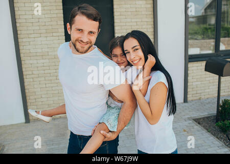 daughter on a piggy back ride with her parents. Mother, father and daughter have a good time near the house Stock Photo