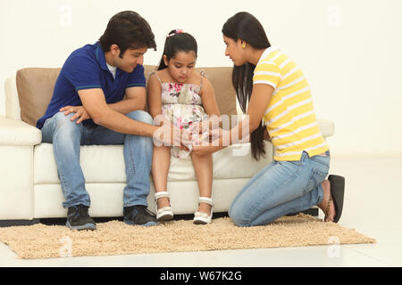 Mother and father putting bandage on daughter,s knee Stock Photo