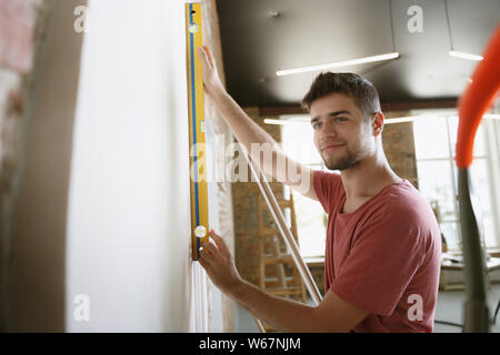 Young man preparing for doing apartment repair by hisselfes. Before home makeover or renovation. Concept of relations, family, DIY. Measuring the wall before painting or design making. Stock Photo