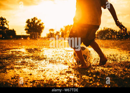 action sport outdoors of kids playing soccer football for exercise in community rural area under the twilight sunset. Poor and poverty children. Stock Photo