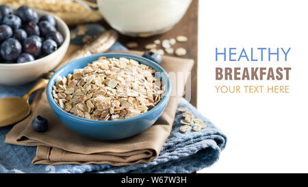 Rolled oats in a blue bowl on a napkin with blueberries, milk and spoon Stock Photo