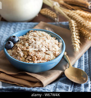 Rolled oats in a blue bowl on a napkin with berries, milk and spoon Stock Photo