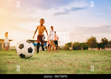 Action sport outdoors of a group of kids having fun playing soccer football for exercise in community rural area . Poor and poverty children. Stock Photo