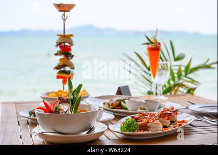 Variety of food, roasted pork ribs, beef steak, seafood and spicy soup on dining table in tropical sea Stock Photo