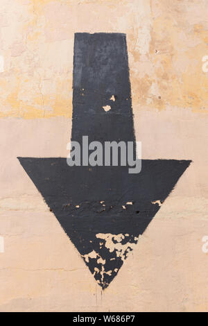 Black aged arrow on concrete wall pointing down Stock Photo