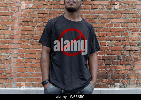 Young attractive man in t-shirt with forbidding prohibition stop symbol on brick background. Stop symbol. Minimalism Stock Photo