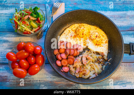 Scrambled eggs with bacon, onion and sausage. In the pan on the table. Stock Photo