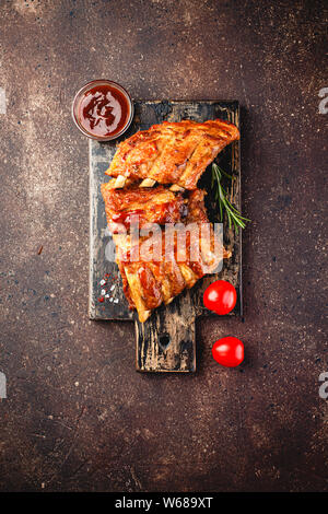 Grilled pork ribs on a wooden cutting board on a brown background. Top view. Stock Photo