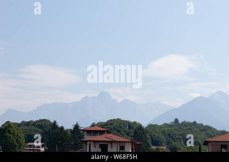Alp mountains behind houses of the town Colico in Como lake district, Italy. Sunny bright summer day.. Stock Photo