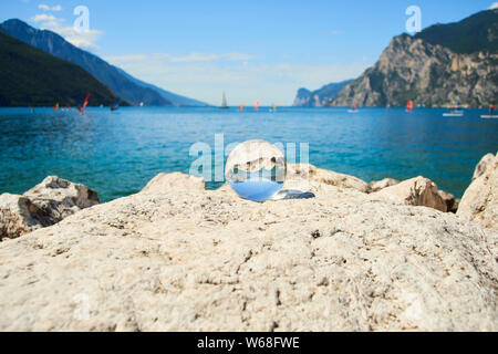 Lake Garda (Lago di Garda or Lago Benaco) seen through a glass crystal  ball placed on rock. Selective focus Stock Photo
