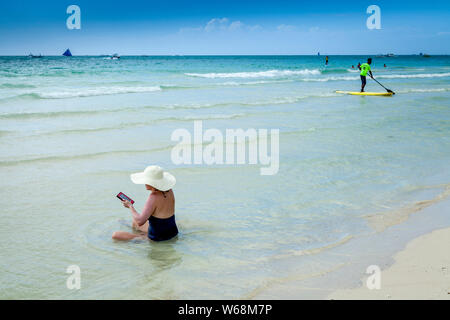 A Woman Sitting In The Sea Reading From  A Kindle, White Beach, Boracay, Aklan, The Philippines Stock Photo