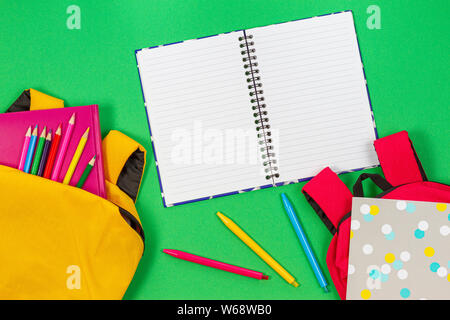 Back to school concept. Two backpacks with school supplies, books and notebooks and open notebook on light green background. Top view Stock Photo
