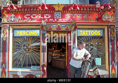 Man checks his phone in front of a piercing and tattoo parlor. Stock Photo