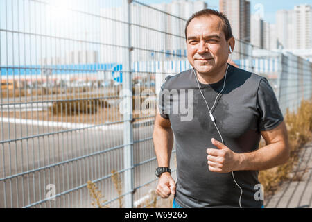 Mature man doing jogging on a city street. Senior man leads a healthy and active lifestyle playing sports. Stock Photo