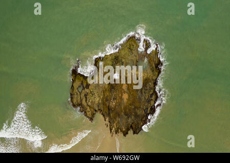 Top down aerial view of a lighthouse on a small rocky island surrounded by a murky, rough sea