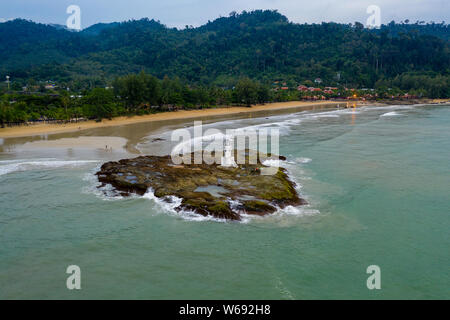 Aerial drone view of a small lighthouse on a rocky island just off a sandy beach and rough sea Stock Photo