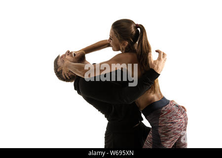 Man in black outfit and athletic caucasian woman fighting on white studio background. Women's self-defense, rights, equality concept. Confronting domestic violence or robbery on the street. Stock Photo