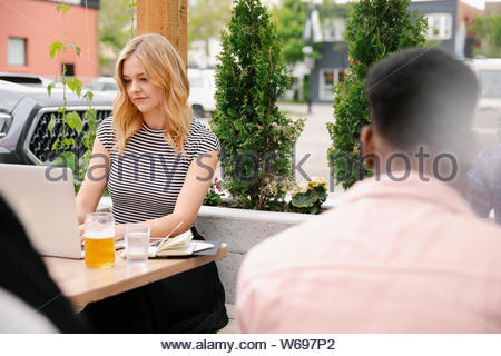 Young woman working at laptop and drinking beer on brewery patio