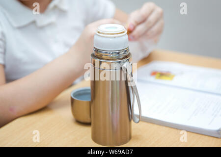 A thermos is sitting on a wooden table . Coffee thermal for school is a must Stock Photo