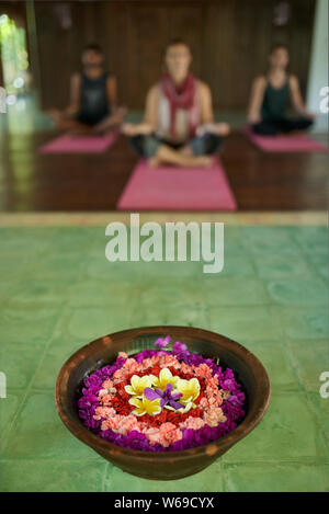 Close up of flower offering for prayer in traditional Indonesian temple in Bali with three diverse people meditating in background Stock Photo