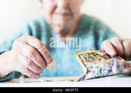 Detailed closeup photo of unrecognizable elderly womans hands counting remaining coins from pension in her wallet after paying bills. Stock Photo