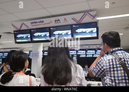Journalists at the media center watch screens display that U.S. President Donald Trump deplanes as his Air Force One arrives at the Paya Lebar Air Bas