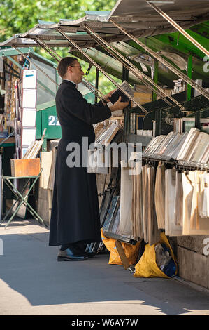 Paris, France - July 04, 2017: A priest in cassock garment searches for a book at a pedestrian book stall by the river Seine. Stock Photo