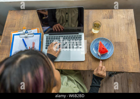 Top view of woman using laptop and eating strawberry cake Stock Photo