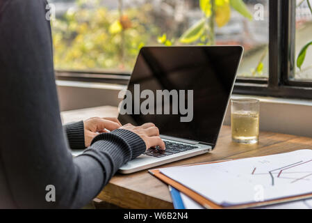 Woman hands typing laptop keyboard at workplace next to window Stock Photo