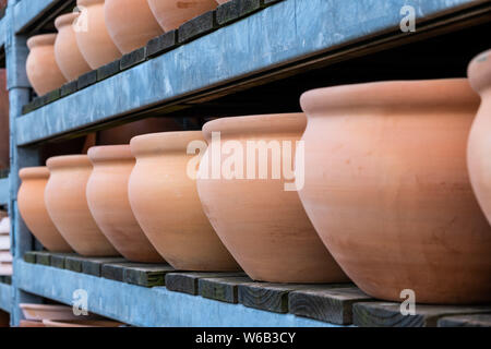Row of large brown clay flower pots on metal shelves Stock Photo