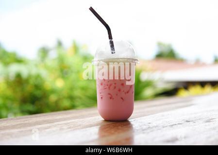 pink strawberry milk pink ice drink in plastic cup juice for summer and straw on wooden table with nature background Stock Photo
