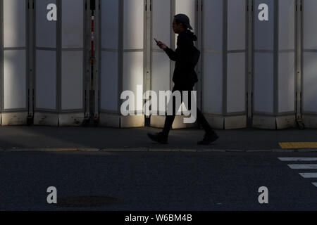 A Japanese man using his smartphone as he walks past a construction site entrance in the streets of Shibuya, Tokyo, Japan. Stock Photo