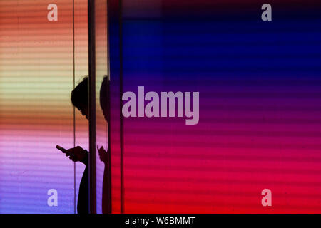 A man in silhouette checks his mobile phone next to a colourful illuminated wall in Shibuya, Tokyo, Japan Stock Photo