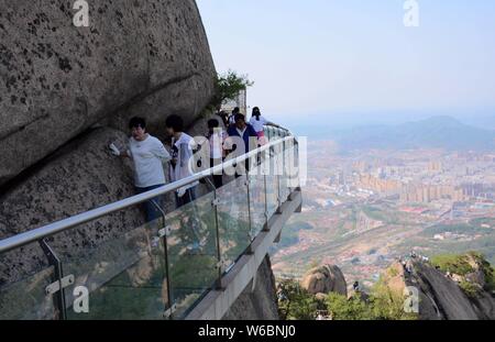 Tourists walk on a glass walkway along the edge of a cliff at Phoenix Mountain in Dandong city, northeast China's Liaoning province, 9 May 2018.   A n Stock Photo