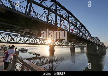 Tourists look far into the distance over Sinuiju of North Korea under the Yalu River Broken Bridge over the Yalu River, also called the Amrok River or Stock Photo