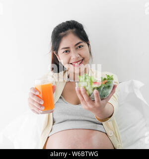 Asian pregnant woman showing eating fruit salad and a glass of orange juice in her hands, lifestyle concept. Stock Photo