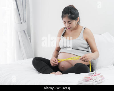 Happy Asian pregnant woman using measuring tape with her belly, lifestyle concept. Stock Photo