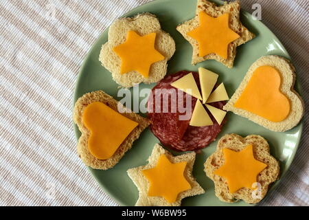 Small canape sandwiches of yellow cheese and toast bread cut in shapes of hearts and flowers served on green plate for kid's party. . Stock Photo