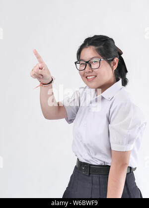 Happy Asian student in uniform pointing something on white background. Stock Photo