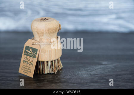 Go Bamboo branded veggie brush with bass fibres, twine tag. Biodegradable materials. Sitting on dark wood grain kitchen bench. Sustainability concept. Stock Photo