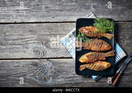 overhead view of pan-fried breaded crucian carps served on a black rectangular plate, flat lay, empty space